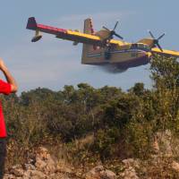 A man takes pictures of a Croatian firefighter plane as it drops water on forest fires on the Lustica peninsula near Tivat, Montenegro, Thursday. Firefighting planes keep flames away from Dubrovnik resort but other Croatia blazes rage on