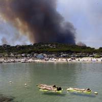 Women sunbathe in Lavandou, French Riviera, as plumes of smoke rise in the air from burning wildfires Wednesday. Authorities ordered the evacuation of 10,000 people as fires hopscotched around the Riviera for a third day Wednesday, tearing through the forest of La Londe-les-Maures. Wildfires force 12,000 in French Riviera to flee, rage also in parched Italy, Portugal