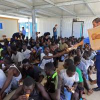 A member of the International Organization for Migration (OIM) distributes food to illegal migrants from Africa, at a naval base in Tripoli after they were rescued by the Libyan coast guard in the Mediterranean Sea off the Libyan coast Monday. Libya rescues 278 Europe-bound migrants in two operations