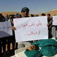 Syrian refugees hold placards as they stand by the body of a Syrian man Tuesday in the town of Arsal, near the Syrian border, in northeast Lebanon. Anger mounted among Syrians in Lebanon Wednesday with at least one Syrian opposition group and an international human rights organization calling for a quick investigation after the death of at least four Syrians in Lebanese army custody. The placard in Arabic (center) reads, “For what crime was he killed? … In Arsal.” Syrians demand probe, autopsies after four die in Lebanese custody following refugee camp sweep