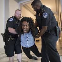 A demonstrator is taken into custody by U.S. Capitol Police as activists protest the Republican health care bill outside the offices of Sen. Jeff Flake, R-Ariz., and Sen. Ted Cruz, R-Texas, Monday on Capitol Hill in Washington. Trump pushes Congress to pass health care overhaul amid impasse as millions more go uninsured
