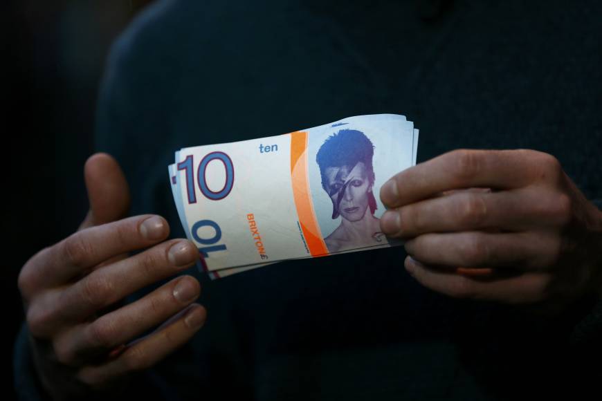 A man holds a 10 Brixton Pounds note, which is decorated with an image of David Bowie.
