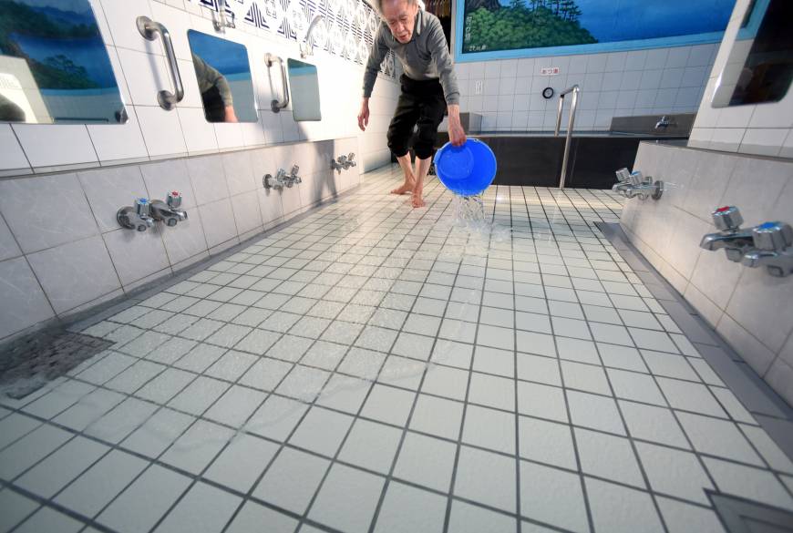Yasuhiro Tsuchimoto, the fourth owner of the Inariyu sento, pours warm water over the floor when the facility opens in the early afternoon to keep bathers