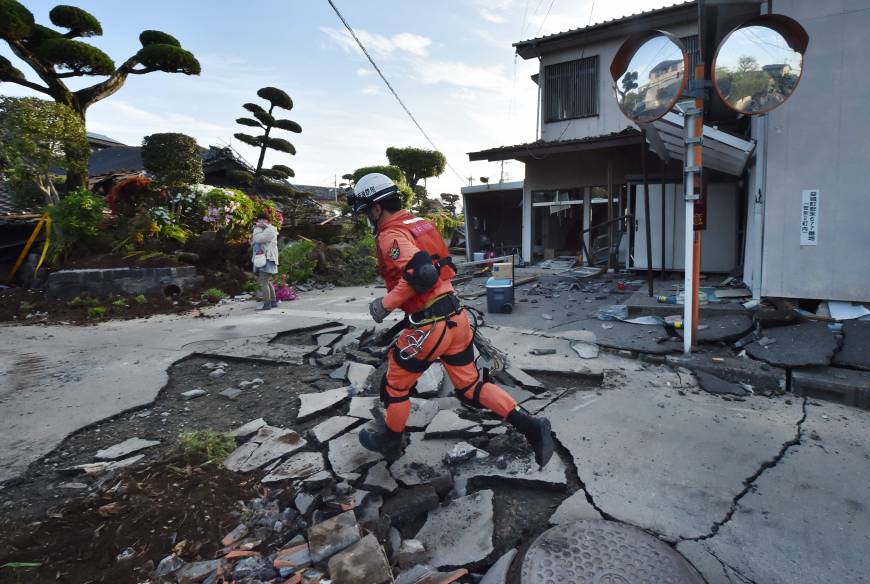 A member of a rescue team runs on a cracked street in  Mashiki, Kumamoto Prefecture on Saturday. 