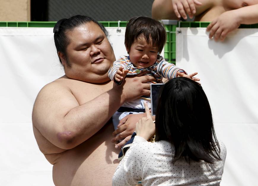 A sumo wrestler hold up a child, who might not be such a big fan now but give it time.