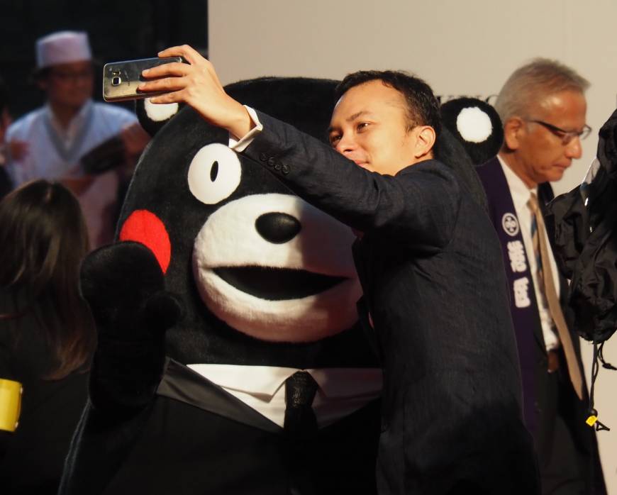 A red carpet participant takes a selfie with Kumamon, who