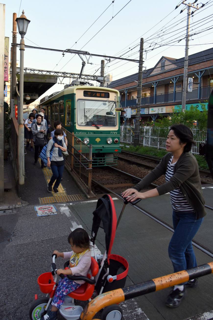 A mother pushes a baby cart across streetcar tracks in Tokyo