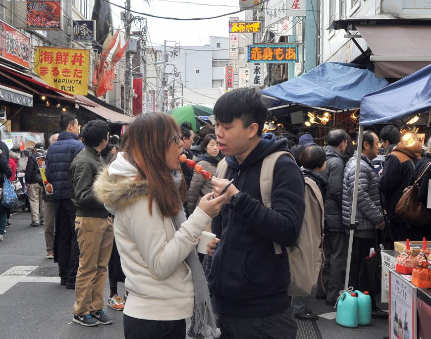 A couple share a strawberry skewer bought at the Tsukiji fish market, which sells not only seafood but also snacks and desserts.
