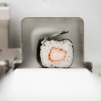 A roll of maki-sushi exits a Suzumo Machinery Co. sushi machine during a demonstration at the company\'s factory. | BLOOMBERG