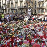 People stand next to flowers, candles and other items set up on the Las Ramblas boulevard in Barcelona as they pay tribute Sunday to the victims of the Barcelona attack, three days after a van plowed into the crowd, killing 13 people and injuring over 100. | AFP-JIJI