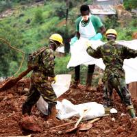 A volunteer and soldiers cover a victim found in the mud and debris, days following the partial collapse of a hillside that swept away hundreds of homes in a neighborhood of the capital Freetown on Sunday. | AFP-JIJI