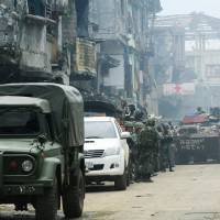 Government troops stand on guard Wednesday in front of damaged buildings and houses after 100 days of intense fighting with insurgents from the Maute Group in Marawi city, in the southern Philippines. | REUTERS