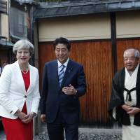 British Prime Minister Theresa May is welcomed by Prime Minister Shinzo Abe and tea master Sen Sosa upon her arrival for a tea ceremony at the Omotesenke school’s Fushinan teahouse in Kyoto on Wednesday. | POOL / VIA AP
