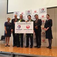 Japan Airlines President Yoshiharu Ueki (center right) and Hawaiian Airlines President and CEO Mark Dunkerley (center left) hold up a board announcing a partnership between the two carriers at a news conference in Tokyo on Tuesday. | ALEX MARTIN