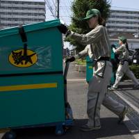 Employees of Yamato Transport Co. push carts loaded with parcels for distribution in Musashimurayama, Tokyo, in May. | BLOOMBERG