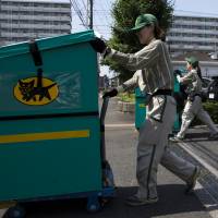 Employees of Yamato Transport Co. push carts loaded with parcels for distribution in Musashimurayama, Tokyo, in May. | BLOOMBERG