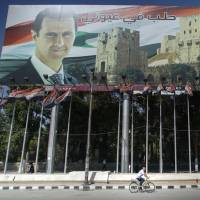 A man rides a bicycle past a billboard depicting Syrian President Bashar Assad, which reads \"Aleppo is in my eyes,\" in the city on Sept. 12. | AP
