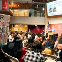 A Harvard University police officer watches a protester holding a sign as U.S. Education Secretary Betsy DeVos talks at a forum at Harvard University\'s Kennedy School of Government in Cambridge, Massachusetts, Thursday. | REUTERS