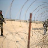 A member of the Palestinian security forces loyal to Hamas stands guard as men set up a barbed wire on the border with Egypt, in Rafah in the southern Gaza Strip, Aug. 24. | REUTERS