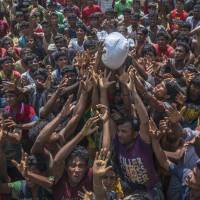 Rohingya Muslims, who crossed over from Myanmar into Bangladesh, attempt to catch a bag of rice thrown at them during distribution of aid near Balukhali refugee camp on Thursday. | AP