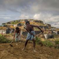 Rohingya Muslim men who crossed over from Myanmar into Bangladesh level the ground before building a shelter at the Balukhali refugee camp Wednesday. | AP