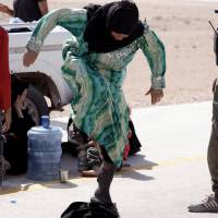 A Syrian woman removes her niqab as she arrives with her family at the Syrian Democratic Forces (SDF) check point in eastern Deir al Zor, Syria, Tuesday. | REUTERS