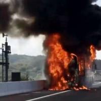 Flames engulf a tour bus on the Shin-Tomei Expressway in Okazaki, Aichi Prefecture, on Saturday after a fire erupted near the engine. No one was injured. | COURTESY OF YASUTOMI KANO / VIA KYODO