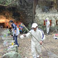 Relatives of Okinawans forced to commit mass suicide in the closing days of World War II clean the Chibichirigama cave, where the suicides took place and where acts of vandalism were discovered earlier this week, in the village of Yomitan on Saturday. | KYODO