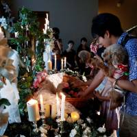 A family carrying their pet dogs places flowers on an altar for a pet dog during a demonstration of pet funeral services at Pet Rainbow Festa, a pet funeral expo held in Tokyo on Monday. | REUTERS