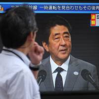 A pedestrian walks past a television screen in Tokyo broadcasting a news report showing Prime Minister Shinzo Abe on Friday after North Korea launched an intermediate-range missile over Japan. | AFP-JIJI