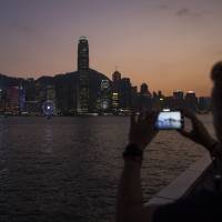 A man takes photographs of Victoria Harbour in Hong Kong. | BLOOMBERG