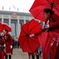 Ushers manage delegates\' umbrellas at the opening session of the Chinese Communist Party congress on Wednesday at the Great Hall of the People in Beijing. | REUTERS