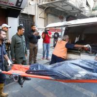 Syrian security forces carry the remains of a reported suicide bomber following an attack near the main police headquarters in Syria\'s capital Damascus on Wednesday. Three suicide bombers blew themselves up near the main police headquarters, killing at least two people, the interior ministry said. | AFP-JIJI