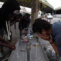 Migrants wash themselves from a sink installed on a street of Paris on Wednesday. Unprecedented waves of migration are affecting the world today, with record numbers of people escaping war-torn regions, poverty, persecution and natural disasters. | AFP-JIJI
