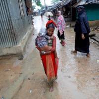A Rohingya girl wearing her holiday dress carries a child through a refugee camp near Cox\'s Bazar, Bangladesh, Sunday. | REUTERS