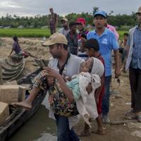 A Bangladeshi man carries Rohingya Muslim woman Rajamma, who crossed over from Myanmar into Bangladesh, toward a boat filled with food aid for stranded refugees in Palong Khali, Bangladesh, Wednesday. Thousands of Rohingya Muslims who crossed the border earlier this week are camping with no or little food and no sanitation, spending days and nights in open fields with just plastic sheets as shelters near zero point of the Bangladesh-Myanmar border. | AP
