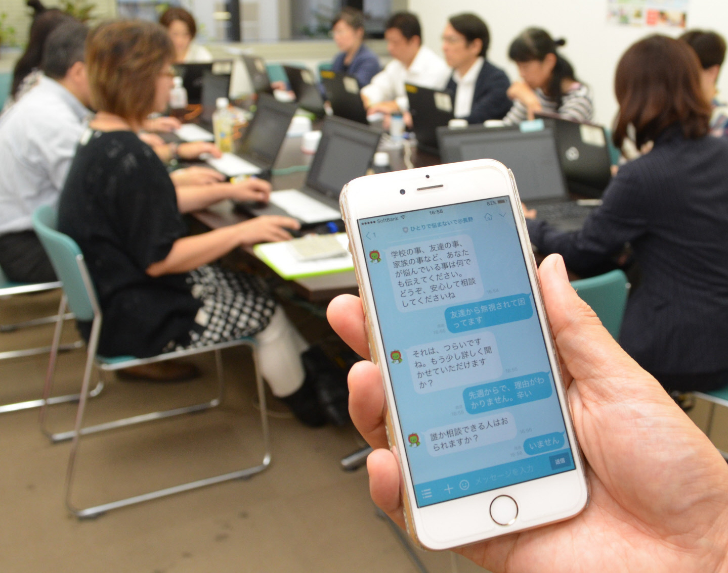 A smartphone screen shows how teenagers can seek consultations with counselors via the Line message app. In the background, counselors respond to them via computers. | CHUNICHI SHIMBUN