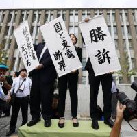 Lawyers representing victims of the Fukushima No. 1 nuclear disaster hold up victory banners in front of the Fukushima District Court on Oct. 10. | KYODO