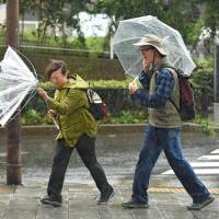 Strong winds turn a woman\'s umbrella inside out in Tokyo on Sunday. A powerful typhoon barreling toward Japan with heavy rains triggered landslides and delayed voting at some ballot stations as millions struggled to get to the polls for a general election. | AFP-JIJI