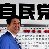 Prime Minister Shinzo Abe smiles before a board of candidates with paper roses who won their seats on Sunday at the Liberal Democratic Party headquarters in Tokyo. | YOSHIAKI MIURA