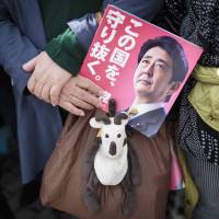 A woman holds an electoral leaflet showing Prime Minister Shinzo Abe during a campaign rally in the city of Saitama on Wednesday. | AFP-JIJI
