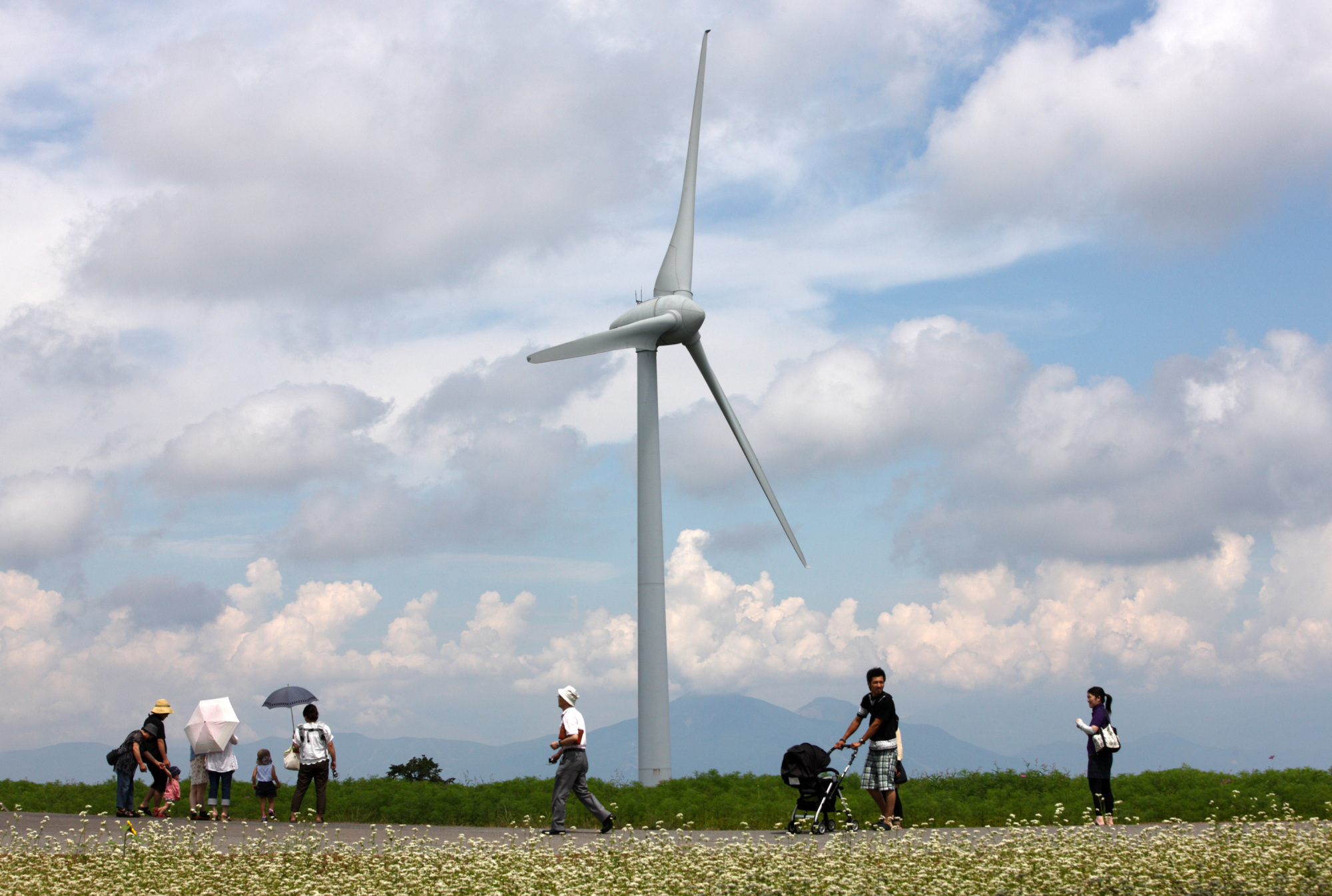People walk past a turbine at the Electric Power Development Co. wind farm near the city of Koriyama, Fukushima Prefecture in August 2012. | BLOOMBERG