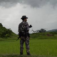 A policeman stands guard on Sept. 27 near a military transport helicopter at Ye Baw Kyaw village in Myanmar\'s northern Rakhine state, where the Myanmar Army claims Rohingya militants massacred scores of Hindu villagers. | AFP-JIJI
