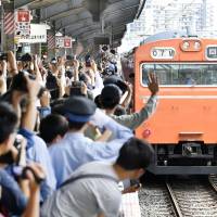 People wave and snap photos as a 103-series commuter train makes its last journey through JR Kyobashi Station in Osaka on Tuesday. The first model of the series was introduced 48 years ago for a loop train network in the city. | KYODO
