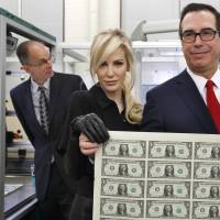 Treasury Secretary Steven Mnuchin and his wife, Louise Linton, hold up a sheet of new &#36;1 bills, the first currency notes bearing his and U.S. Treasurer Jovita Carranza\'s signatures, on Wednesday at the Bureau of Engraving and Printing in Washington. | AP