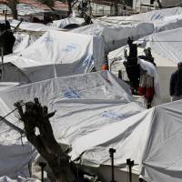 A migrant stands between tents at the Moria refugee detention center on the northeastern Greek island of Lesbos in March. Authorities on Lesbos have called for residents to strike during anti-government protests to press for a change in the European Union policy of containment of refugees and migrants on the Greece\'s islands that have turned Lesbos into an \"island prison,\" according to island authorities. | AP