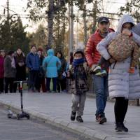 A woman carries a child as they arrive at the RYB kindergarten in Beijing on Friday. RYB Education fired the head of one of its kindergartens in the capital as well as a 22-year-old female teacher following allegations of child abuse at a facility run by the U.S.-listed company. | AP