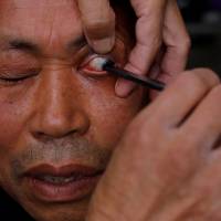 A customer looks on as Xiong Gaowu, a 62-year old street barber, cleans his eye using the straight razor in Chengdu, in southwest China\'s Sichuan province, on Nov. 18. | REUTERS