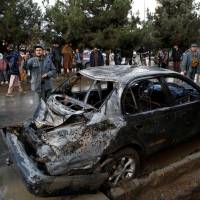 People look on at a damaged vehicle after a suicide bomb attack in Kabul Thursday. | REUTERS