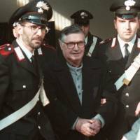 Handcuffed Mafia \"boss of bosses\" Salvatore \"Toto\" Riina is escorted by Italian paramilitary police into a bunker courtroom in Bologna in January 1996. | AP